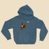 Hoodie featuring a cartoon creature wearing a raincoat, life jacket, and rain boots while carrying two umbrellas and staring nervously at a single cloud overhead.