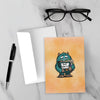 But What If greeting card featuring a worried blue monster clutching an overflowing binder labeled “But What If?” against a warm orange background.