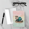 Greeting card featuring a blue furry monster building a tower of office supplies beside a laptop while a calendar full of crossed-off days hangs in the background.