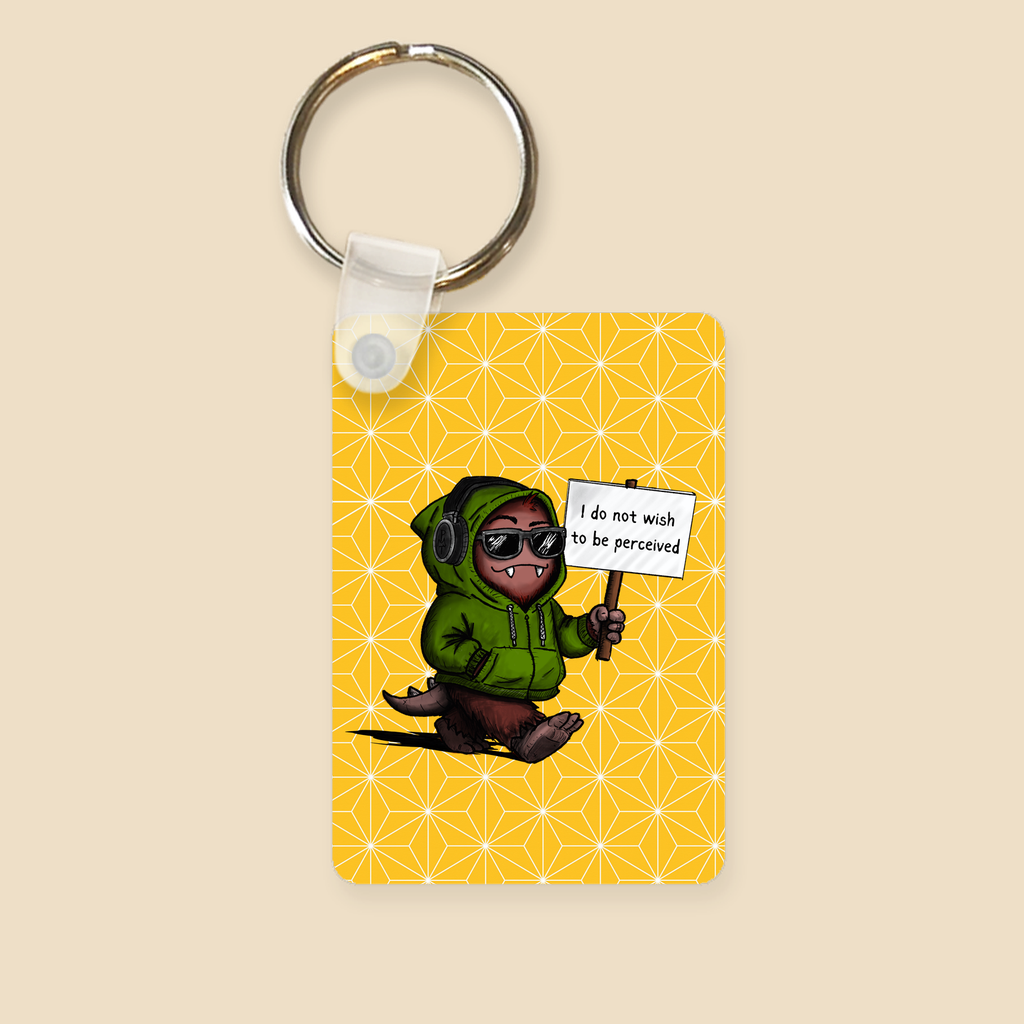 Double-sided keychain featuring a cartoon creature in sunglasses holding a sign reading “I do not wish to be perceived” on a yellow background with geometric star details.