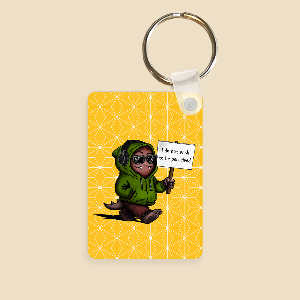 Double-sided keychain featuring a cartoon creature in sunglasses holding a sign reading “I do not wish to be perceived” on a yellow background with geometric star details.