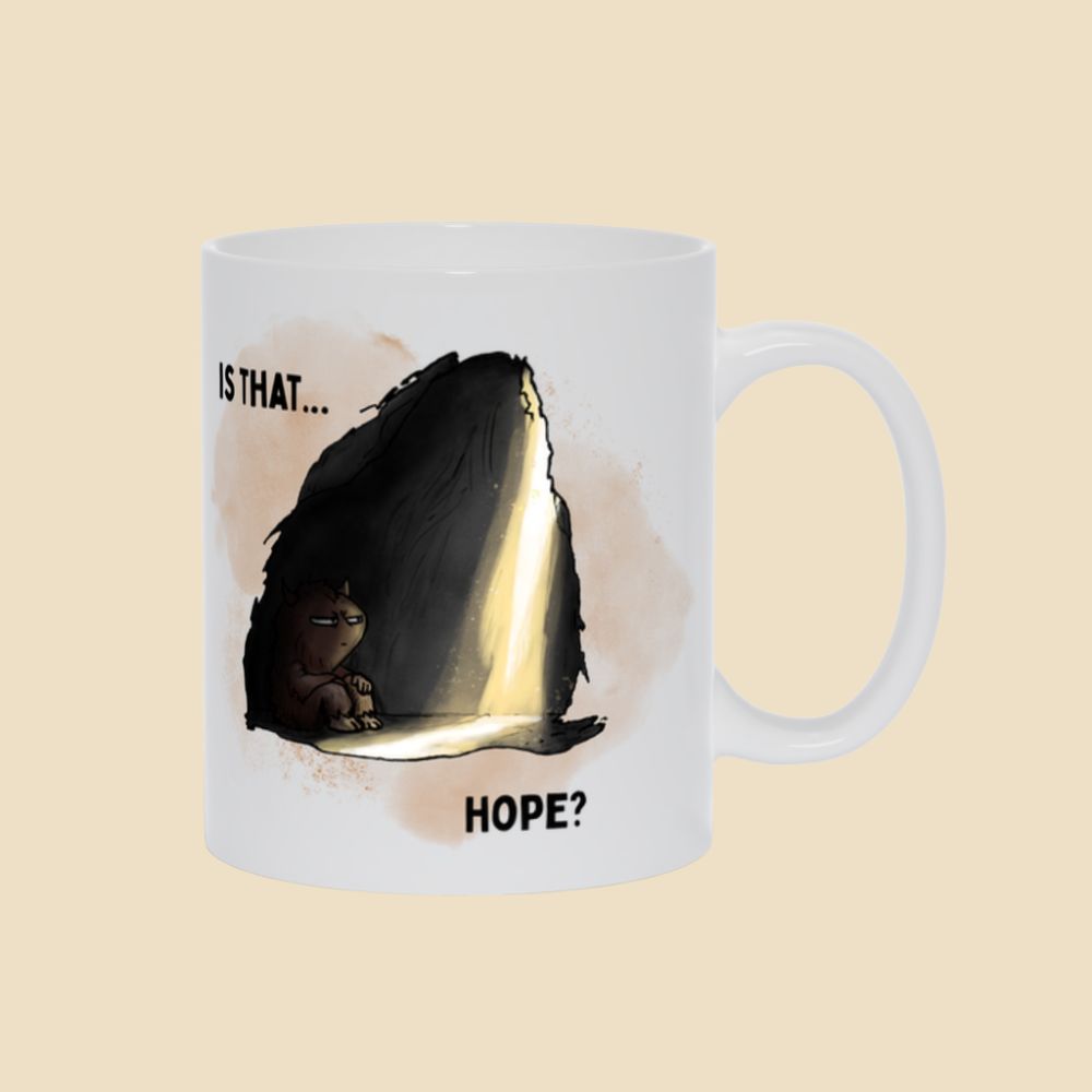 White mug featuring the “Is That… Hope?” depression humor design with a small illustrated monster sitting inside a dark cave as a beam of light shines in.