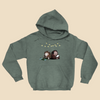 Hoodie featuring two cartoon creatures sitting back to back beneath string lights, one working on a puzzle and the other writing in a notebook.