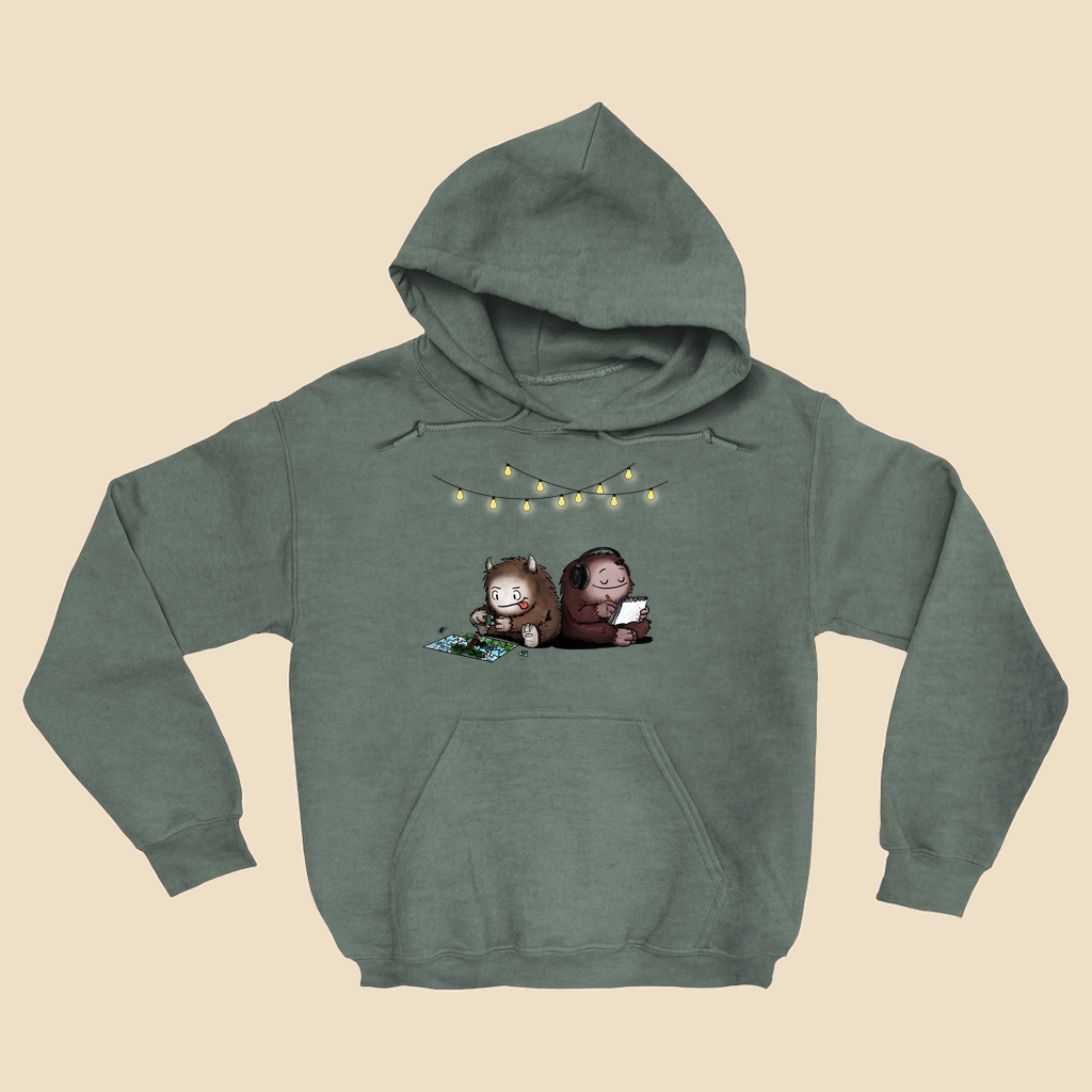 Hoodie featuring two cartoon creatures sitting back to back beneath string lights, one working on a puzzle and the other writing in a notebook.