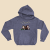 Hoodie featuring two cartoon creatures sitting back to back beneath string lights, one working on a puzzle and the other writing in a notebook.