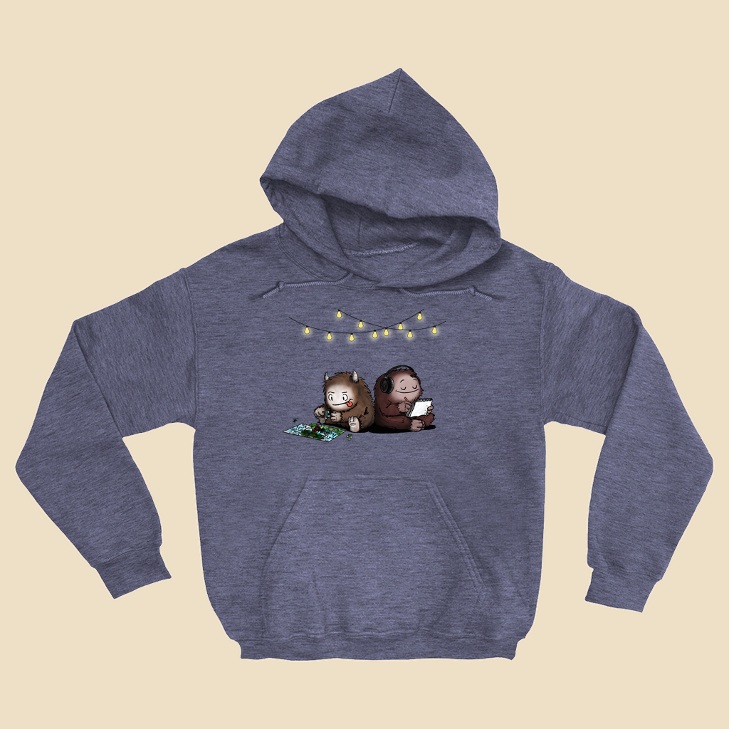 Hoodie featuring two cartoon creatures sitting back to back beneath string lights, one working on a puzzle and the other writing in a notebook.