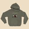 Hoodie featuring two cartoon creatures sitting back to back beneath string lights, one working on a puzzle and the other writing in a notebook.