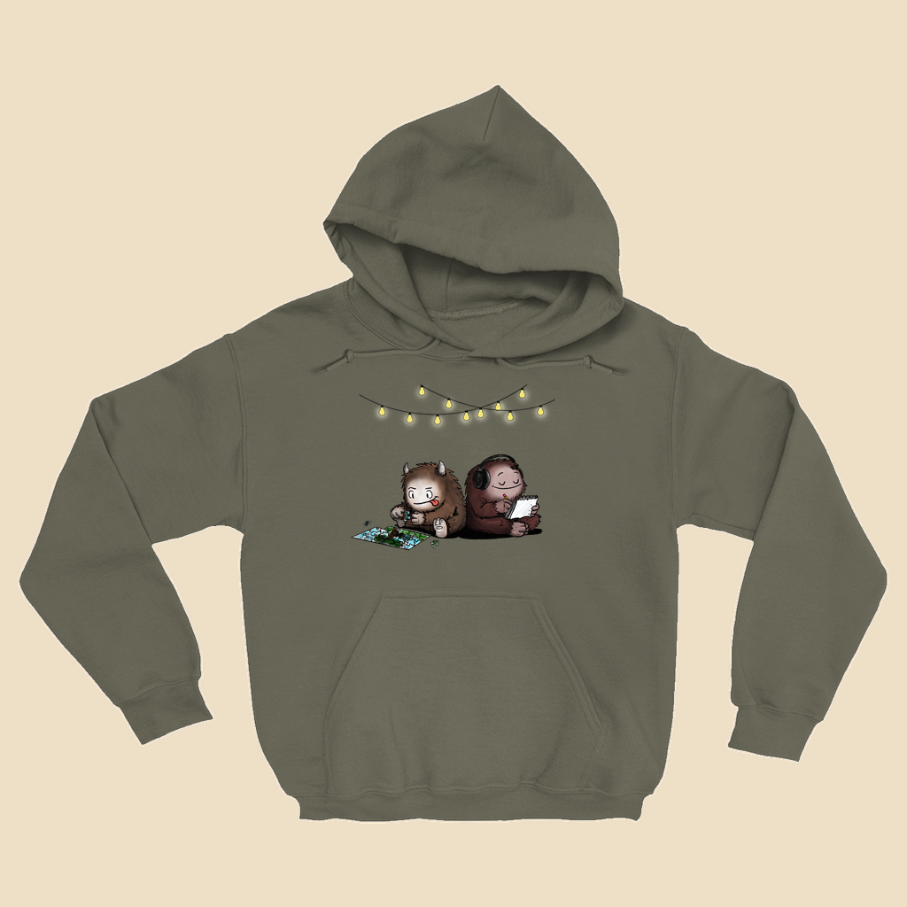 Hoodie featuring two cartoon creatures sitting back to back beneath string lights, one working on a puzzle and the other writing in a notebook.