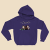 Hoodie featuring two cartoon creatures sitting back to back beneath string lights, one working on a puzzle and the other writing in a notebook.