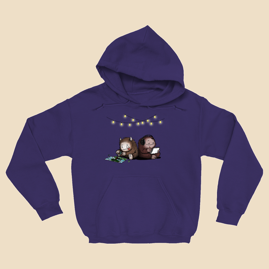 Hoodie featuring two cartoon creatures sitting back to back beneath string lights, one working on a puzzle and the other writing in a notebook.