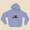 Hoodie featuring two cartoon creatures sitting back to back beneath string lights, one working on a puzzle and the other writing in a notebook.
