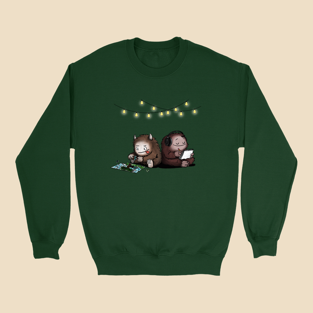 Sweatshirt featuring two cartoon creatures sitting back to back beneath string lights, one working on a puzzle and the other writing in a notebook.