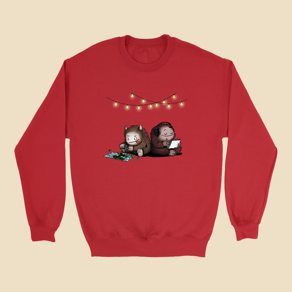 Sweatshirt featuring two cartoon creatures sitting back to back beneath string lights, one working on a puzzle and the other writing in a notebook.