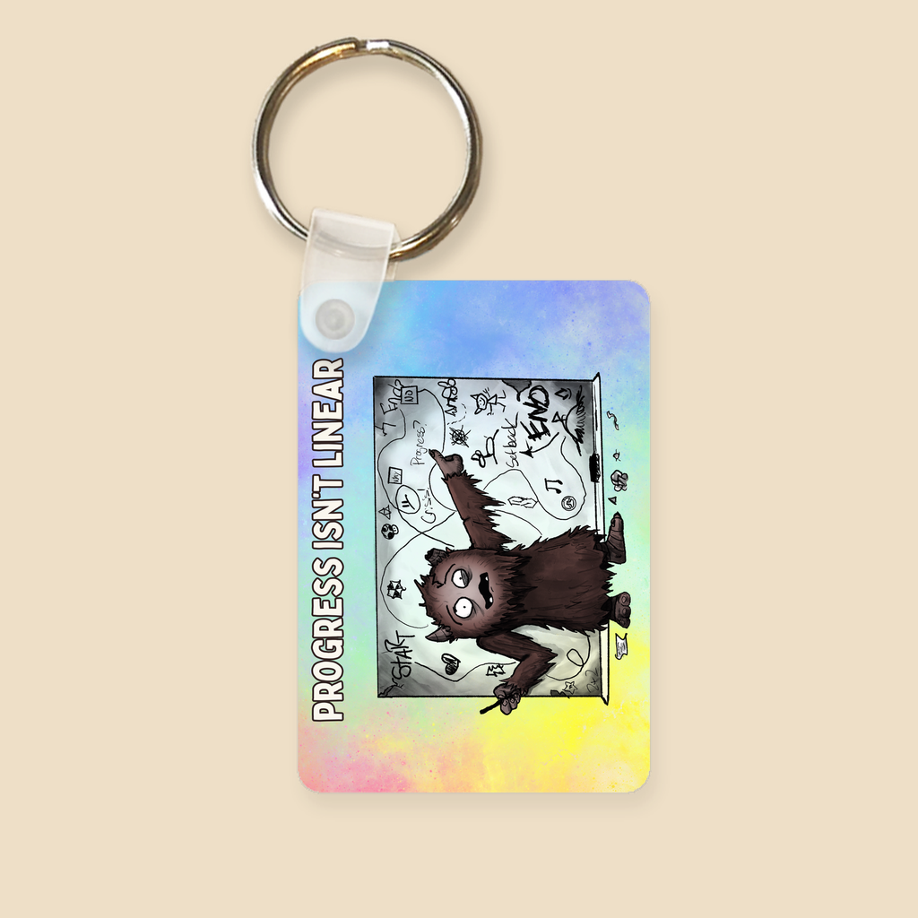 Progress Isn’t Linear keychain featuring a furry brown monster pointing at a messy, winding progress chart filled with twists, turns, setbacks, and doodles.