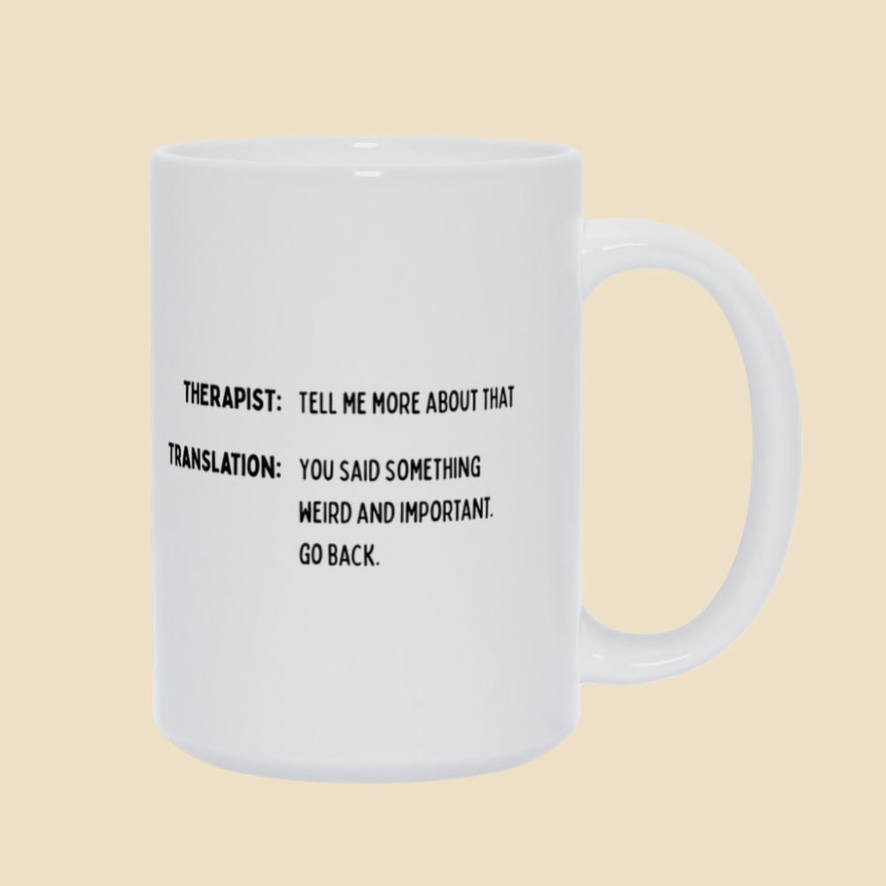 White mug with black text reading “Therapist: Tell me more about that. Translation: You said something weird and important. Go back.”